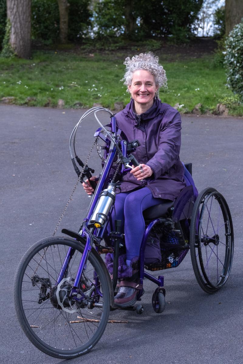 A woman smiles at the camera seated on a three-wheel hand cycle