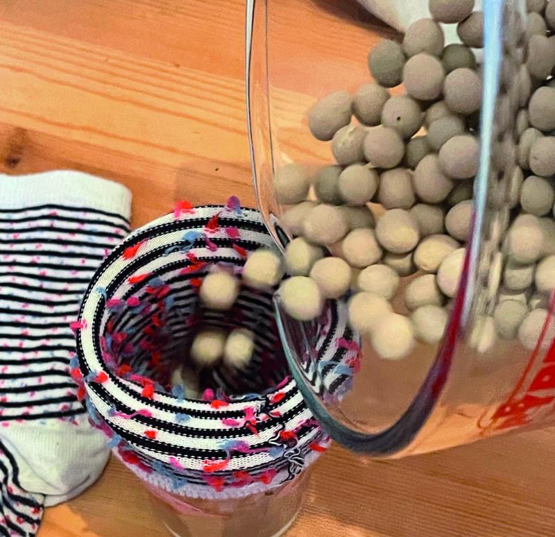 ceramic baking beans are being poured from a glass jar into the inside of socks