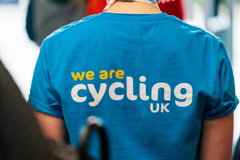 A close-up of a person wearing a light blue T-shirt with the words 'We are Cycling UK' printed on the back