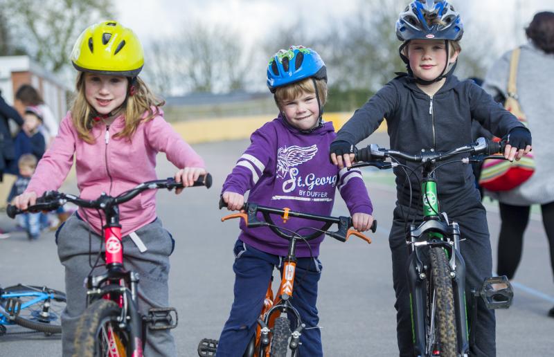 Three young children are standing astride bikes and smiling into the camera