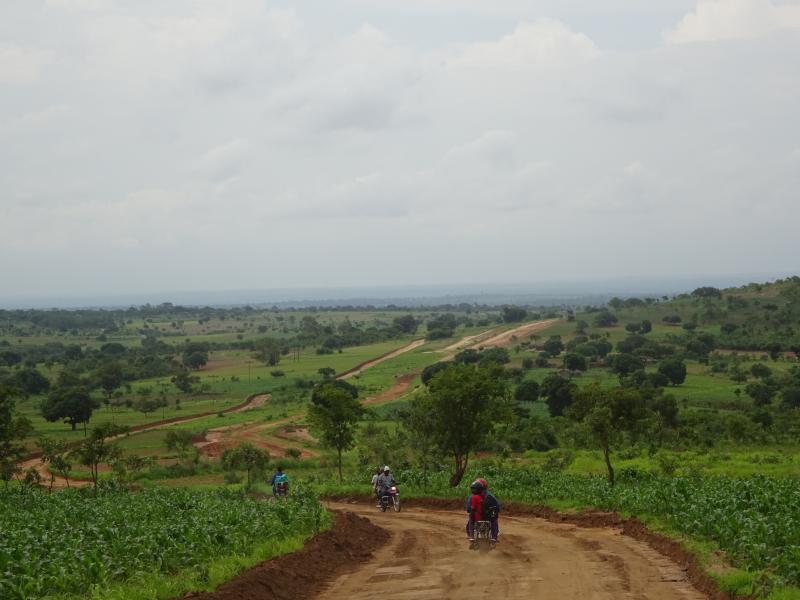 People are riding bikes along a dirt track though African countryside