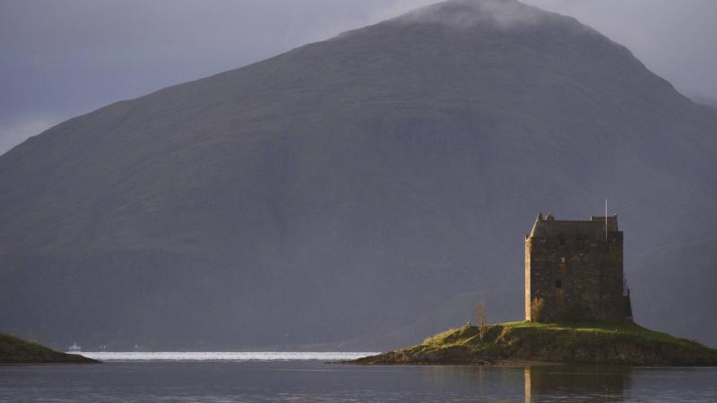 A ruin on an island in a loch with a mountain in the background