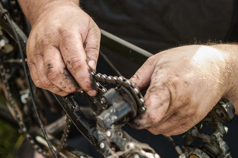 A close-up of a dirty bike chain and two hands holding it