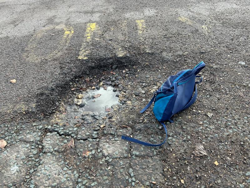 A rain-filled pothole in a country road with a blue rucksack next to it showing the size of the hole