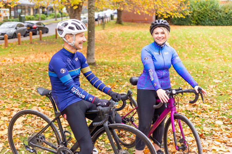 Two people are sitting astride their road bikes, while wearing Cycling UK-branded kit from Stolen Goat