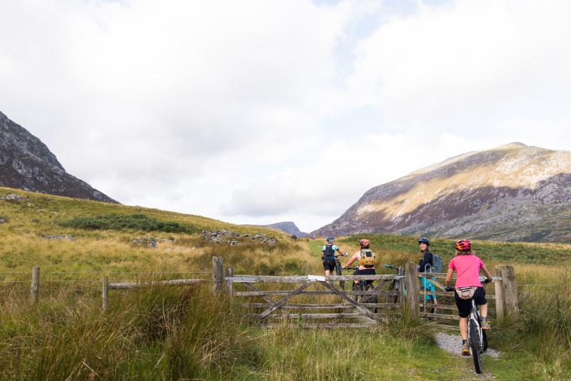 4 cyclists on the Traws Eryri route in North Wales going through a gate with mountains in the distance