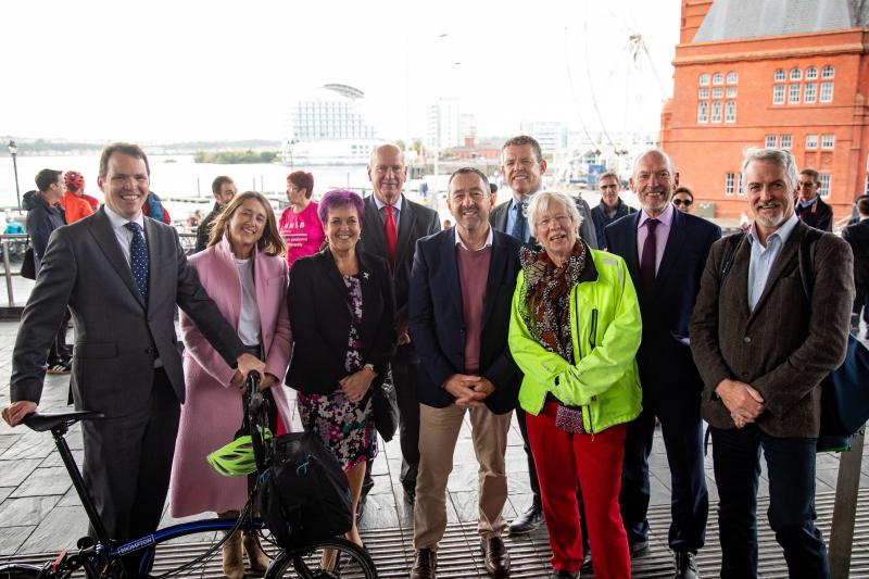 A group of people which includes Chris Boardman are standing and smiling to the camera