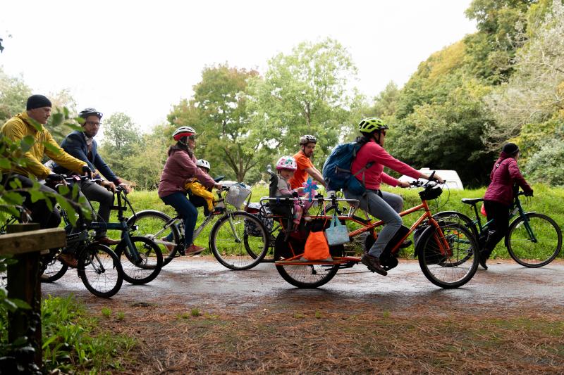 A mixed group of people are cycling along a paved path in a park