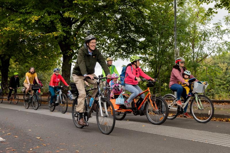 A mixed group of people, including babies in child seats, are cycling along a segregated cycle path