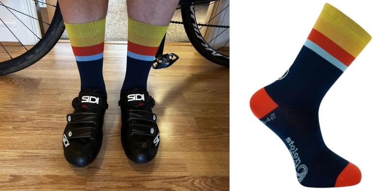 Composite image of Stolen Goat Iowa Thermolite Crew Socks with someone wearing them while standing on a wood floor, wearing Sidi cycling shoes and bike wheels just seen in the background (right) and the sock which is dark blue with red toe and heel and yellow, red and light blue stripes around the cuff.