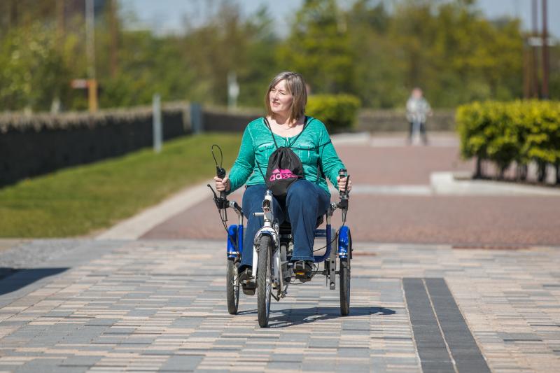 A women cycling a recumbent trike out in the sun on a pedestrianised path