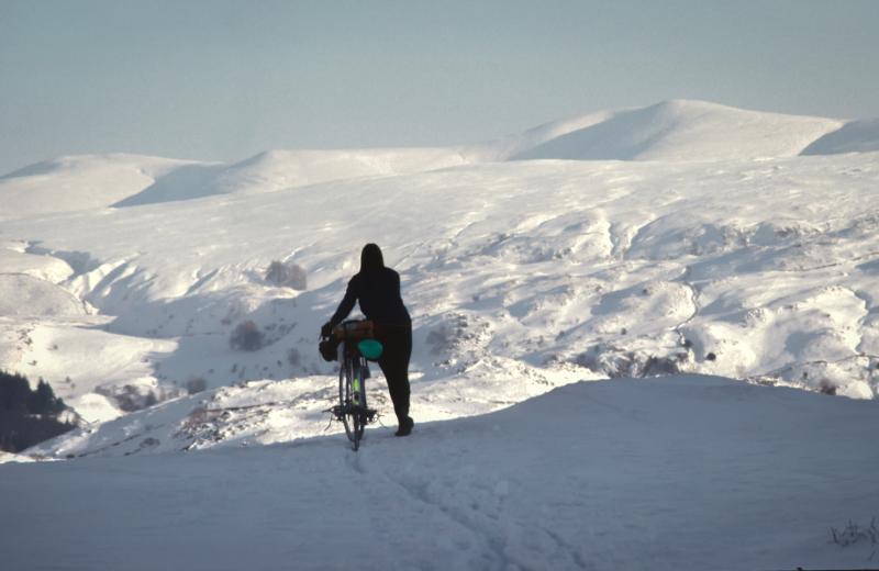 A cyclist standing on a snowy plateau