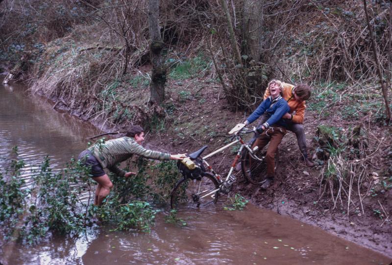 A cyclist is helped pulling their bike out of a river