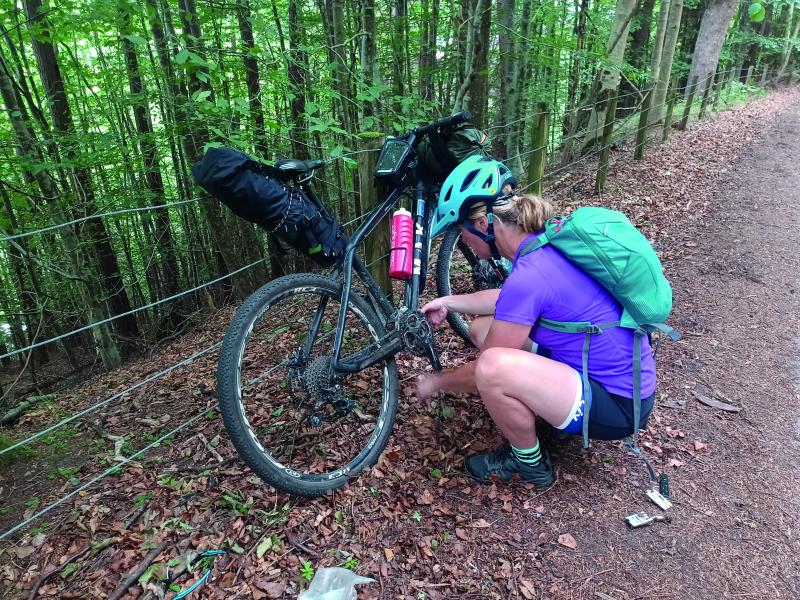 A woman is crouching down working on her bicycle