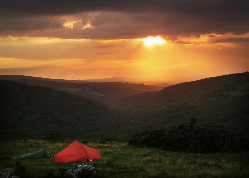 Small tent pitched on a hillside at sunset