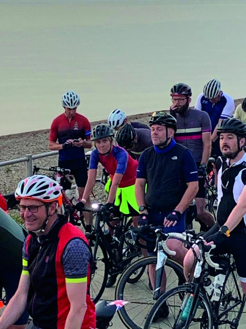 A group of cyclists pose on a beach. They're poised ready to start a long-distance bike ride