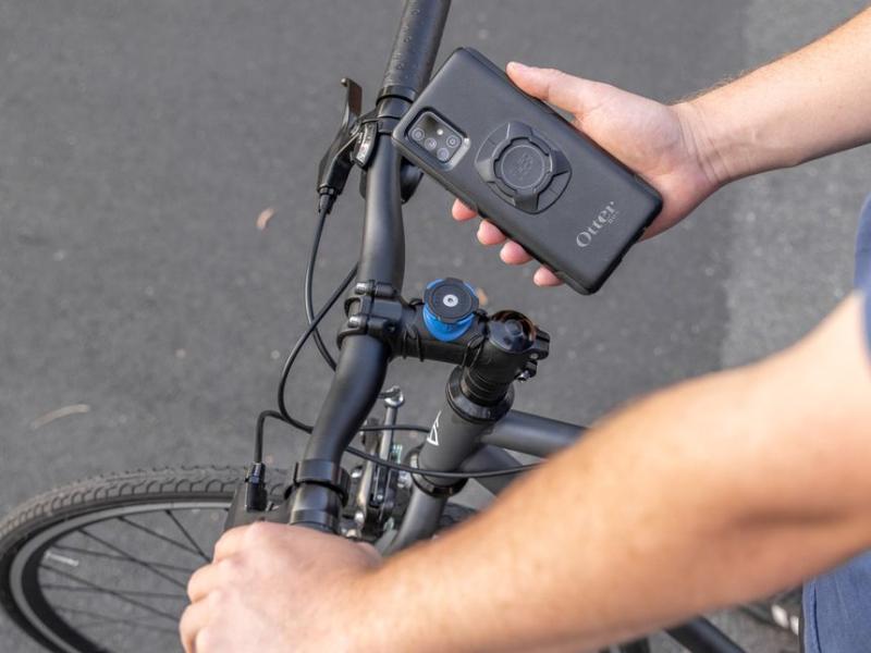 A black phone case with a slot in the back for a handlebar mount. There is a phone mount on a bicycle stem
