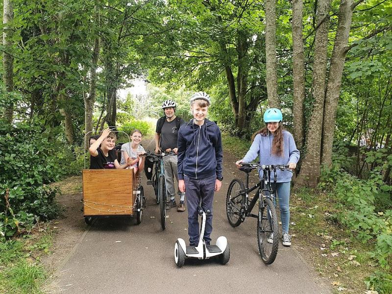 Small group of adults and children on a woodland cycle path with bikes, a cargo bike and a segway
