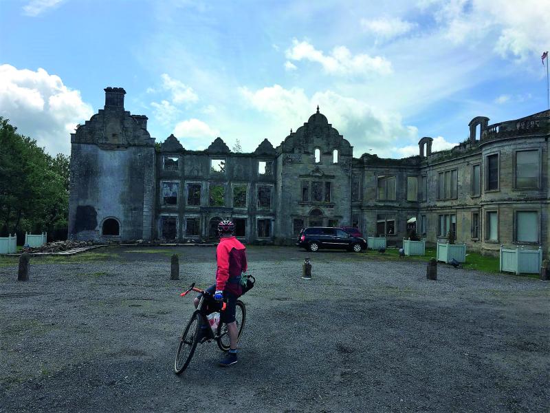 Alf stands with his bicycle admiring the ruins of a great stately home in the background