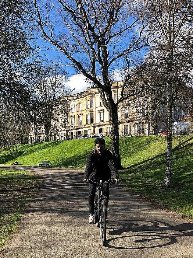 A man cycles towards us along a path in an urban park