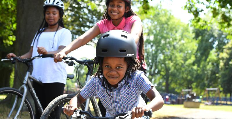 A young boy on a bike grinning with two girls on bikes beside him