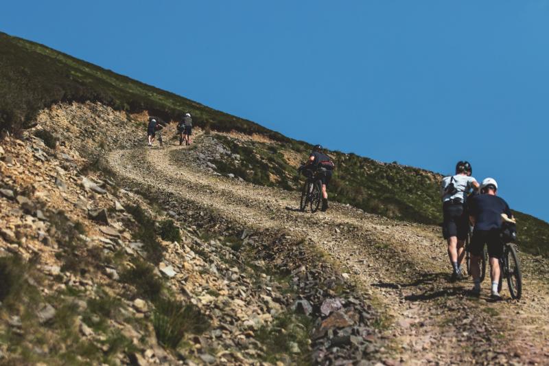 People push bikes up a steep rocky track