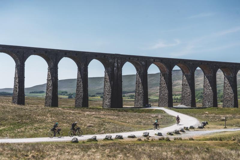 Four cyclists pass beneath the huge Ribblehead Viaduct in the Yorkshire Dales