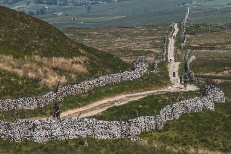 People cycle up a long gravel track, which extends a long way behind them into the distance