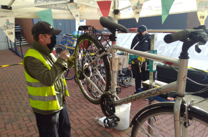 An outdoor cycle repair session, a blue barge with yellow lettering can be seen in the background