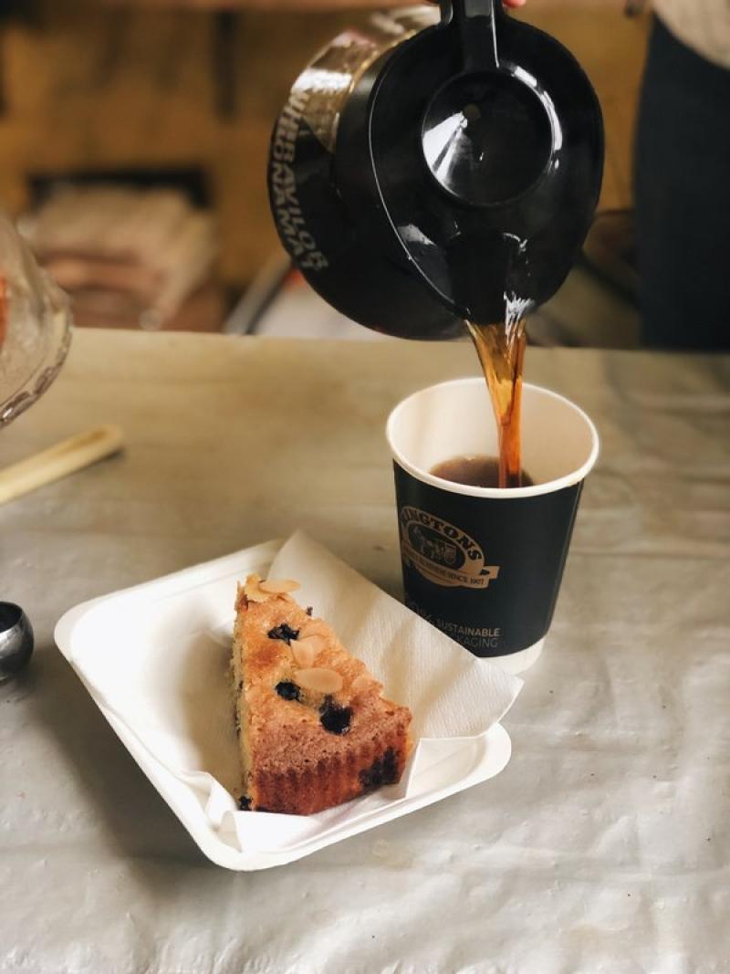 A cup of coffee being poured from a filter pot and a piece of cake on a table