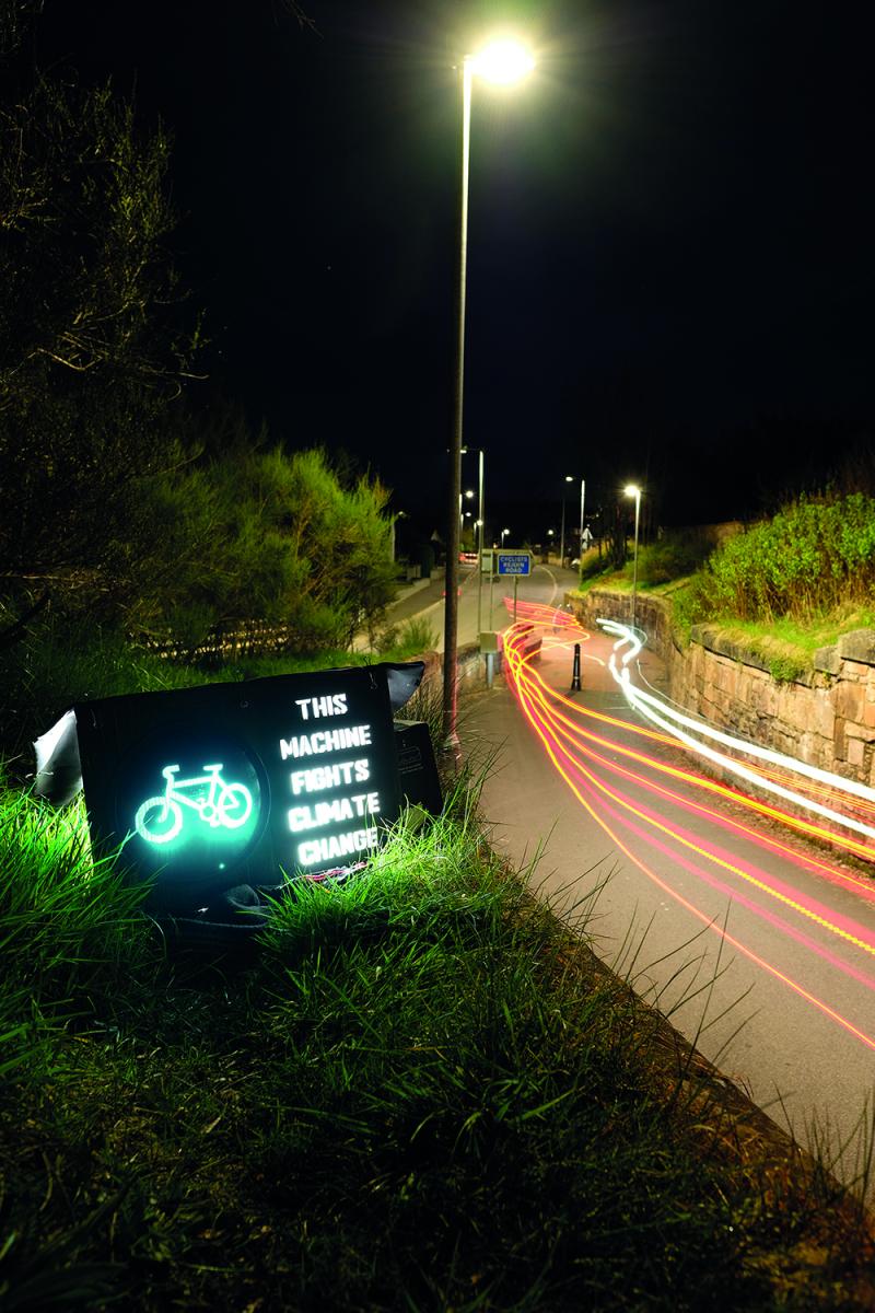An illuminated sign next to a cycle lane reads 'This machine fights climate change'