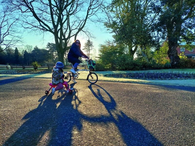 A woman and her child cycle on separate bikes in a park on a dry, cold winter's day