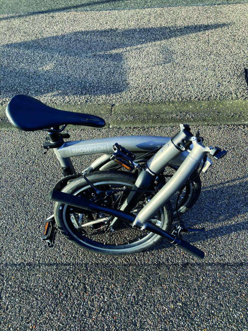 The Brompton bicycle in it's folded state. It is folded up on itself three times to stand saddle-up on the ground in a compact size