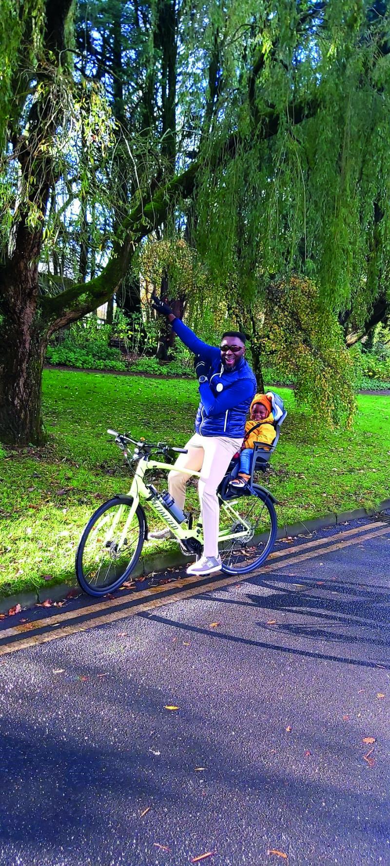 A man sits astride an e-cycle carrying a child in a seat behind him