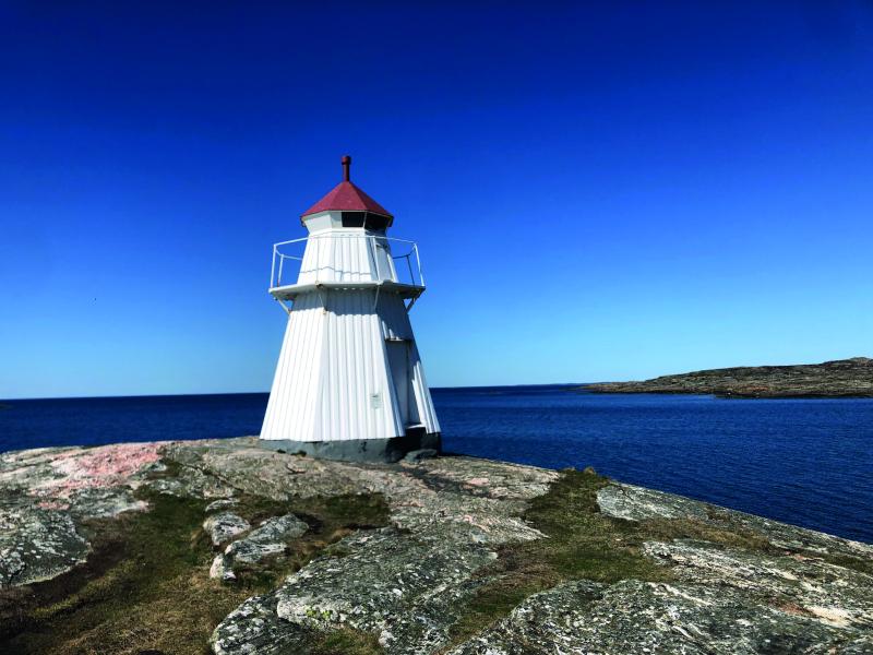 A white Swedish lighthouse stands alone on a rocky coastline