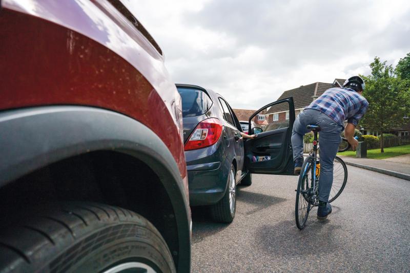 A man riding a bicycle swerves round a car door as the driver opens it