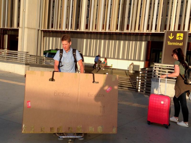 A man pushes a cardboard box labelled bike on an airport trolley