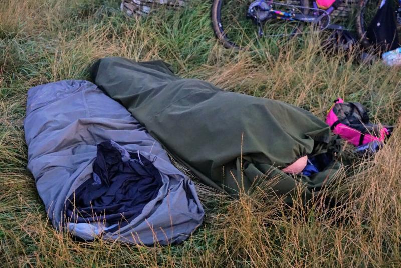 Two bivvy bags with one sleeper laid out in a field