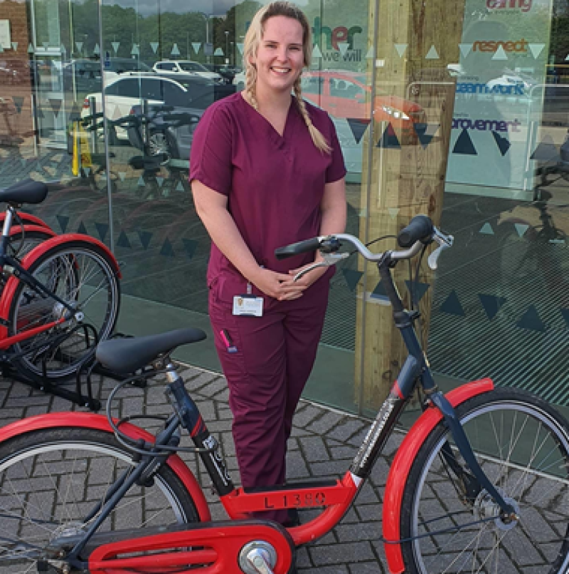 A blonde woman with purple healthcare workers' uniform stood with a red bicycle