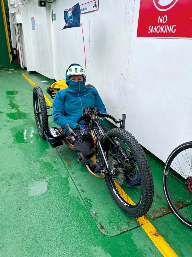 Neil sits in his hand cycle. He looks quite cold wrapped up in a waterproof jacket aboard a ferry