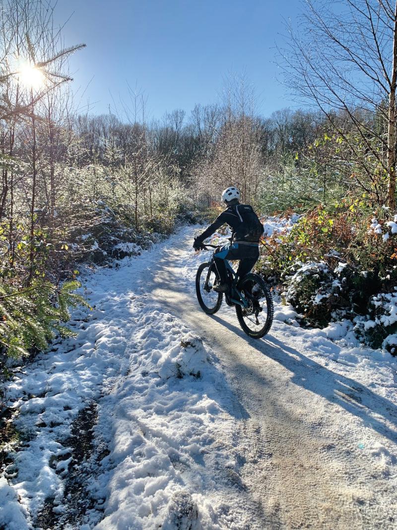 A woman cycles away from camera into a snowy scene