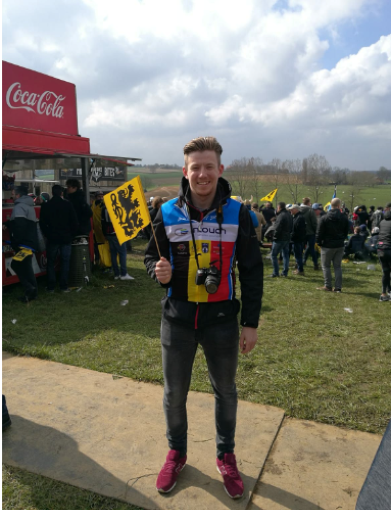 A young man in a cycling jersey with a Belgian flag on the chest holding a yellow flag with a lion emblem on it