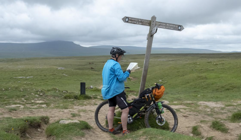 A cyclists stops to look at a map at a crossroads sign in the countryside