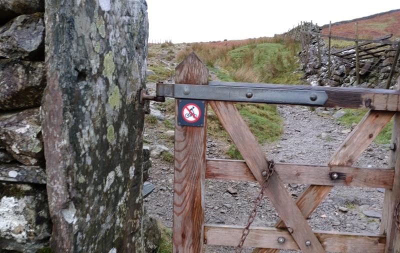Small sign on a countryside gate showing a mountain biker with a red line through, indicating no cycling