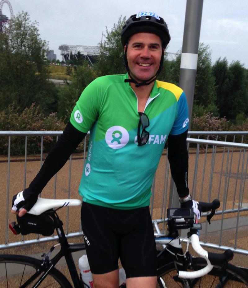 A man wearing a cycling helmet and a bright green top poses by his bicycle