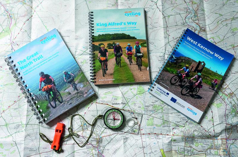 Three Cycling UK route guides lay on a paper map with a compass and whistle