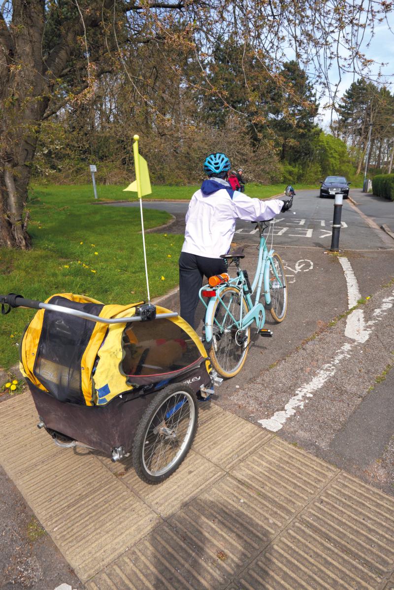 A woman pushes a bicycle that is towing a child trailer along a cycle lane