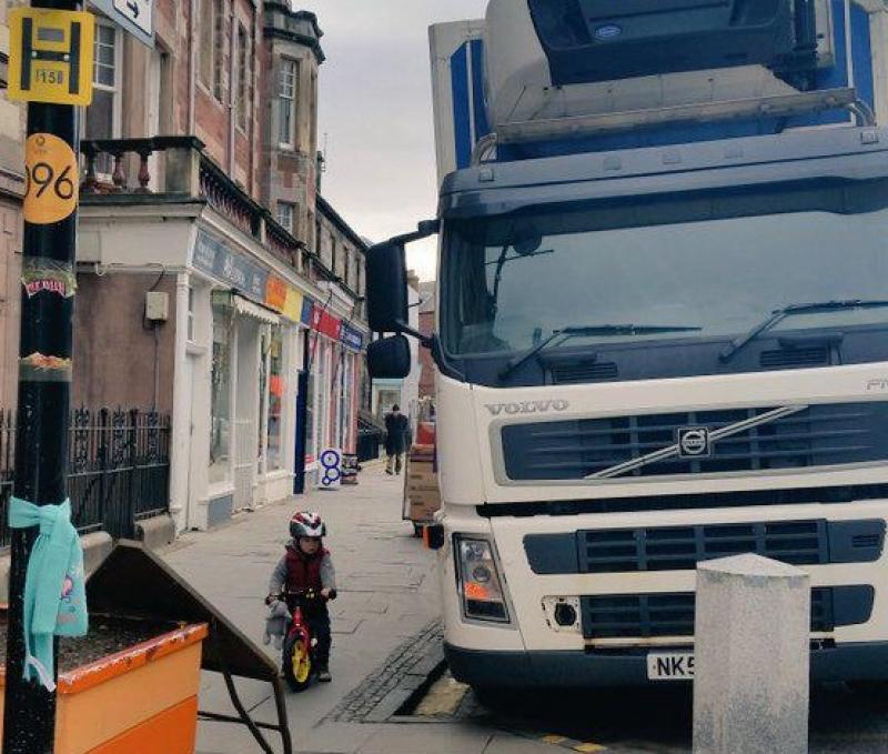 A small child on a balance bike beside a huge lorry