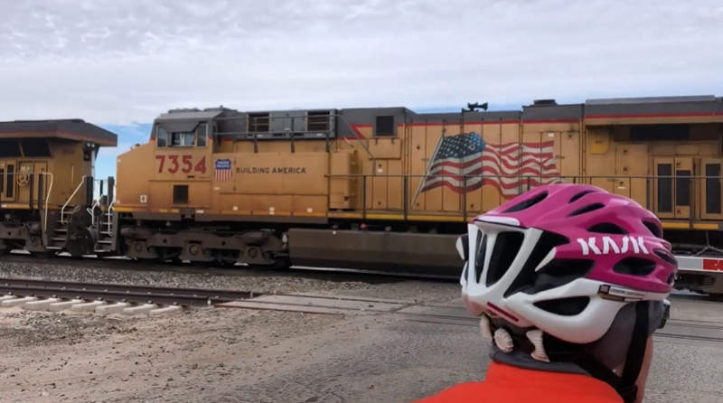 A view of a large yellow freight train with a stars and stripes flag rolling past