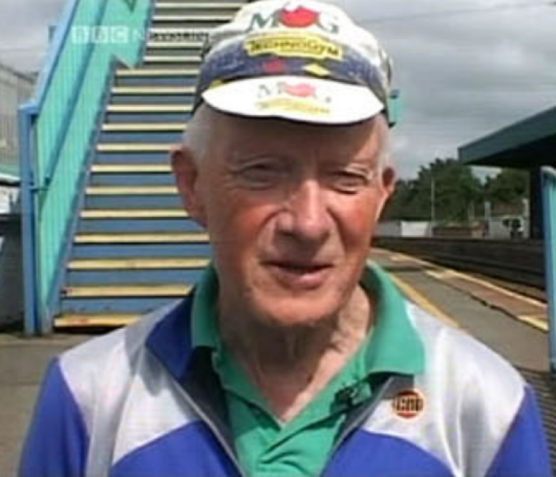 A close up of the face of a man with a cycling cap standing on a railway platform